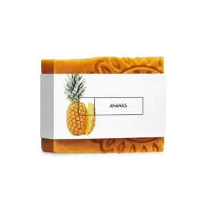 Naturalne pomarańczowe mydło w kostce ownięte białą minimalistyczną etykietą zawierającą nazwę i zdjęcie ananasa