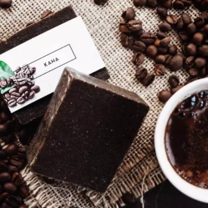 Brązowe kostki naturalnego kawowego mydła leżą na obrusie w towarzystwie świeżo zaparzonej kawy i rozsypanych ziaren